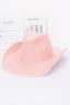 Pink cowboy hat on a white surface with a newspaper in the background