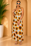 Woman wearing a sunflower patterned dress in a warm-toned room with a plant.