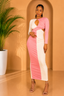 Woman in a pink and white dress standing against a beige wall with a plant to her left.