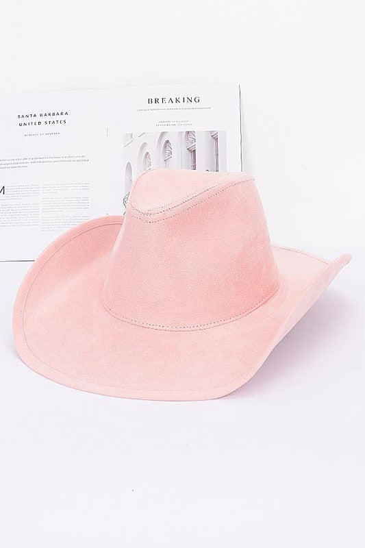Pink cowboy hat on a white surface with a newspaper in the background