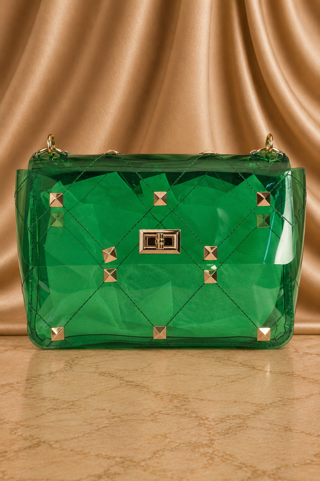 A translucent green quilted handbag with gold-tone studs and a central clasp, set against a draped gold satin background.