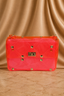 A bright neon pink quilted nylon shoulder bag with gold pyramid studs and a central gold-tone logo clasp, set against a draped beige satin background.