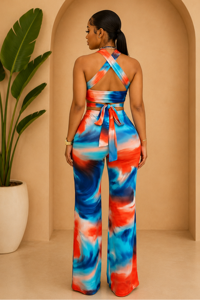 Woman wearing a colorful tie-dye jumpsuit standing in front of a beige wall with an arch.