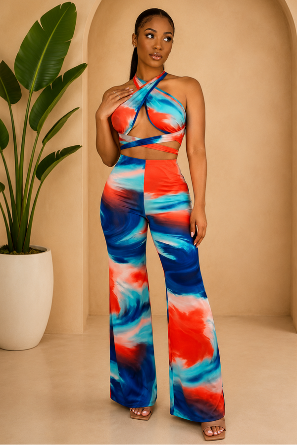 Woman wearing a colorful tie-dye outfit standing in a beige room with a plant.