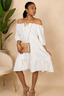 Woman in a white dress holding a colorful handbag against a beige background