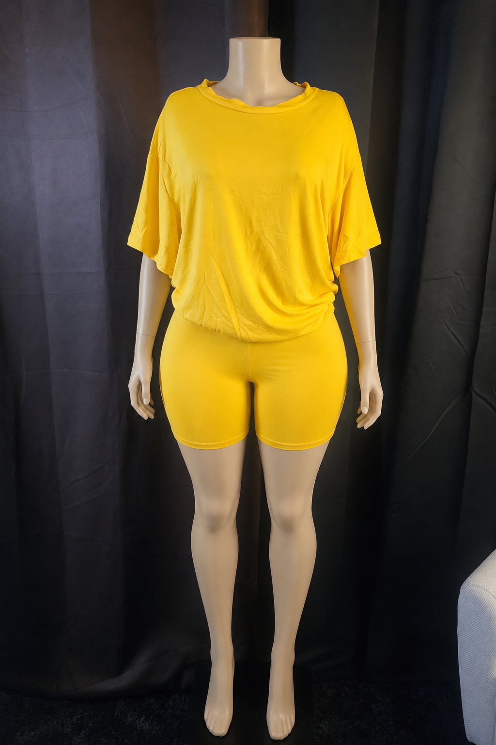 A bright yellow two-piece lounge set consisting of a short-sleeve cropped t-shirt and matching high-waisted shorts, displayed on a mannequin against a black fabric backdrop.