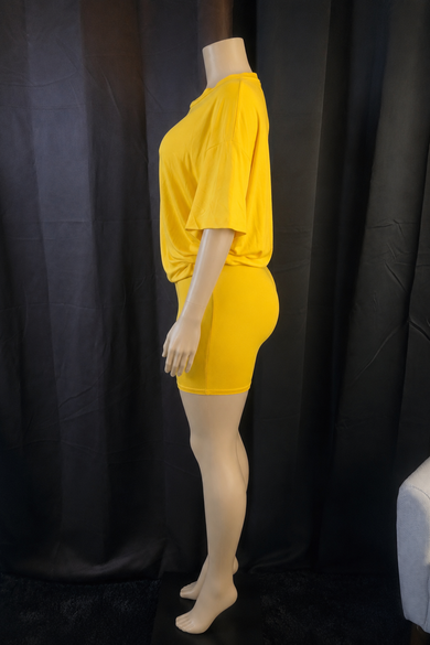 A mannequin wearing a bright yellow two-piece outfit consisting of a loose short-sleeve top and matching fitted mini skirt, photographed against a black curtain backdrop.