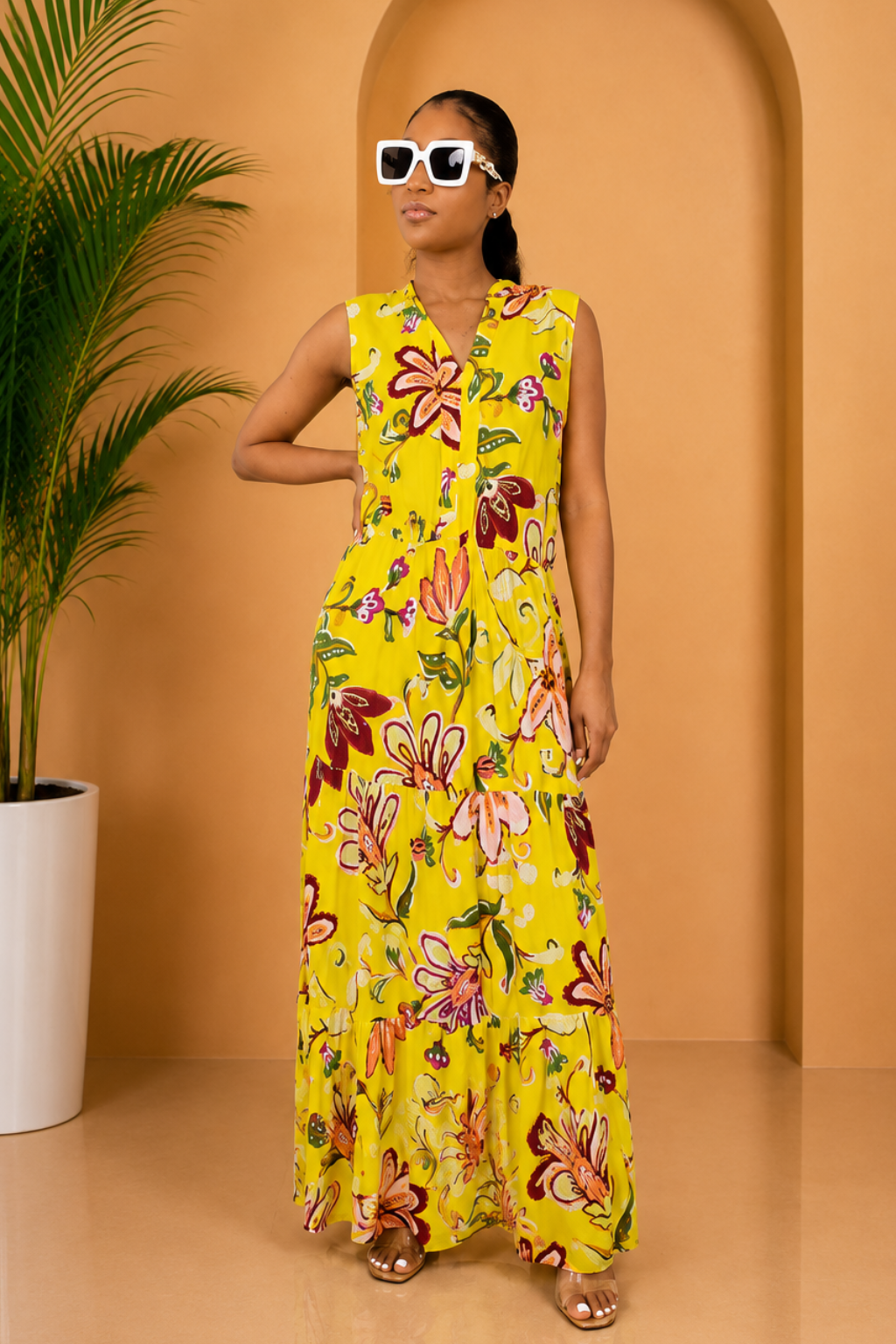 Woman in a yellow floral dress standing in front of an archway with a plant to the side.
